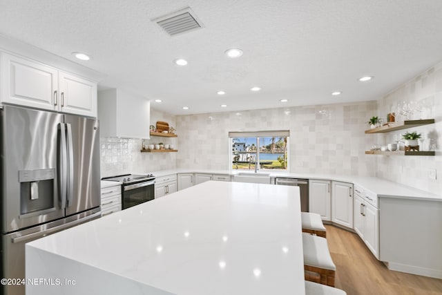 kitchen featuring white cabinets, a kitchen breakfast bar, backsplash, and appliances with stainless steel finishes