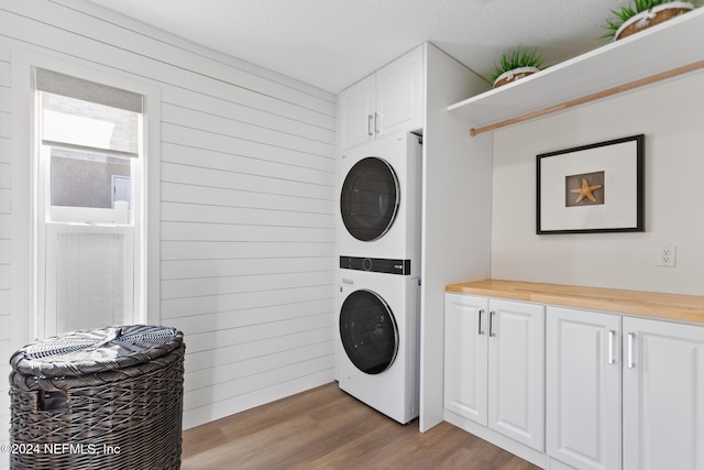 laundry area featuring cabinets, stacked washing maching and dryer, light hardwood / wood-style floors, and wood walls