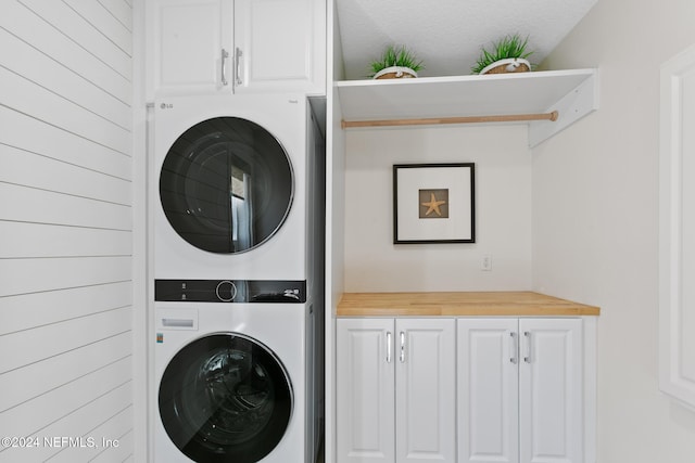 clothes washing area with cabinets and stacked washer and clothes dryer