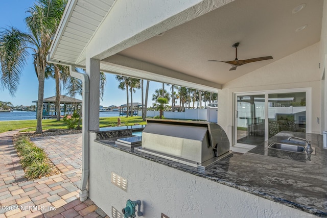 view of patio featuring grilling area, an outdoor kitchen, a water view, sink, and ceiling fan