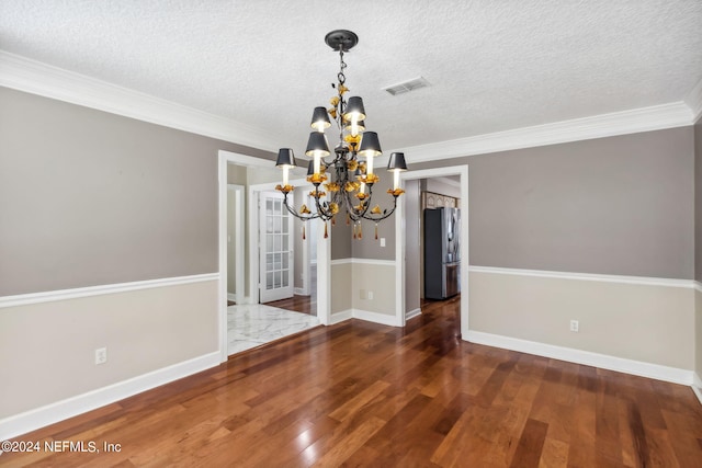 unfurnished dining area with a textured ceiling, dark hardwood / wood-style floors, an inviting chandelier, and ornamental molding