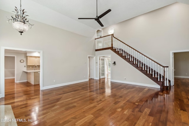 unfurnished living room with ceiling fan with notable chandelier, dark hardwood / wood-style flooring, and high vaulted ceiling