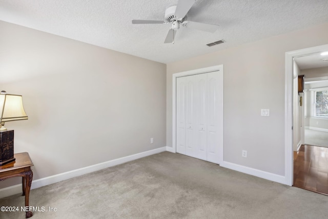 unfurnished bedroom featuring ceiling fan, a closet, light colored carpet, and a textured ceiling