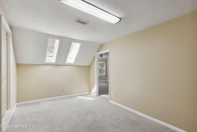 additional living space featuring a textured ceiling, light carpet, and lofted ceiling with skylight