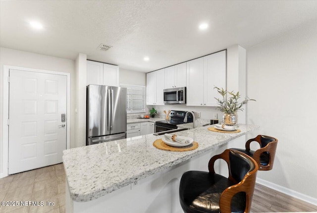 kitchen featuring light stone counters, stainless steel appliances, visible vents, white cabinetry, and a peninsula