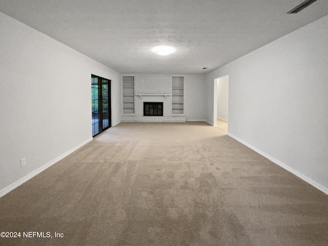 unfurnished living room with built in features, carpet floors, a textured ceiling, and a brick fireplace