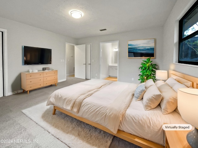 carpeted bedroom with ensuite bathroom and a textured ceiling