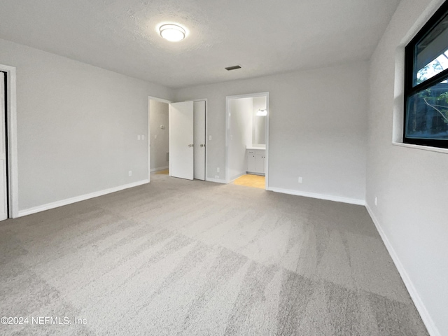 unfurnished bedroom with carpet, a textured ceiling, and ensuite bath