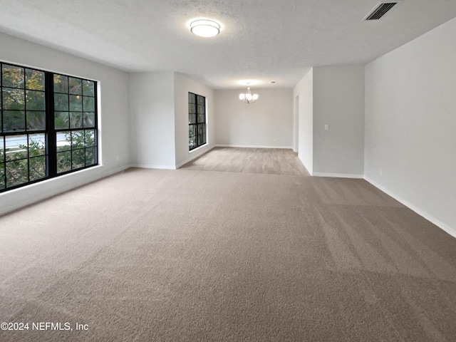 empty room with light carpet, a textured ceiling, and an inviting chandelier