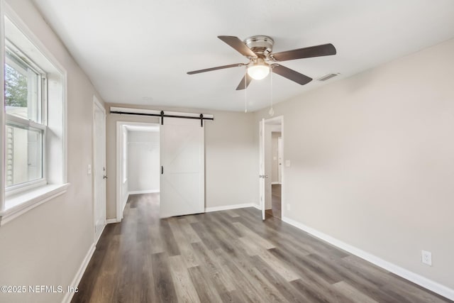 unfurnished bedroom featuring ceiling fan, a barn door, wood-type flooring, and a closet