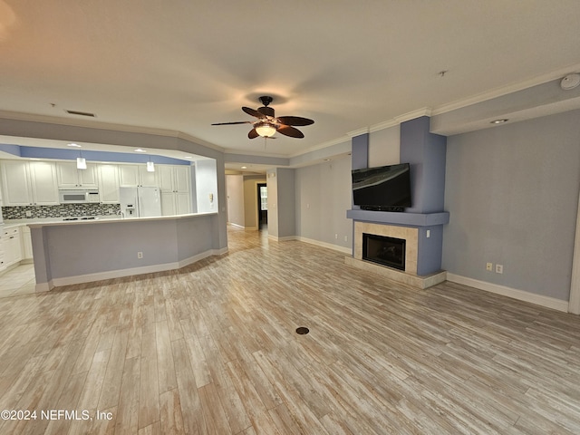 unfurnished living room with a tiled fireplace, crown molding, ceiling fan, and light hardwood / wood-style floors