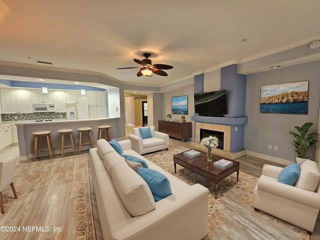 living room with crown molding, ceiling fan, a tile fireplace, and light hardwood / wood-style flooring