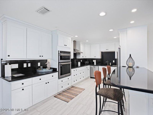 kitchen featuring backsplash, white cabinetry, wall chimney exhaust hood, and appliances with stainless steel finishes