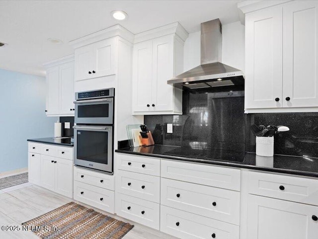 kitchen featuring double oven, decorative backsplash, white cabinetry, and wall chimney exhaust hood