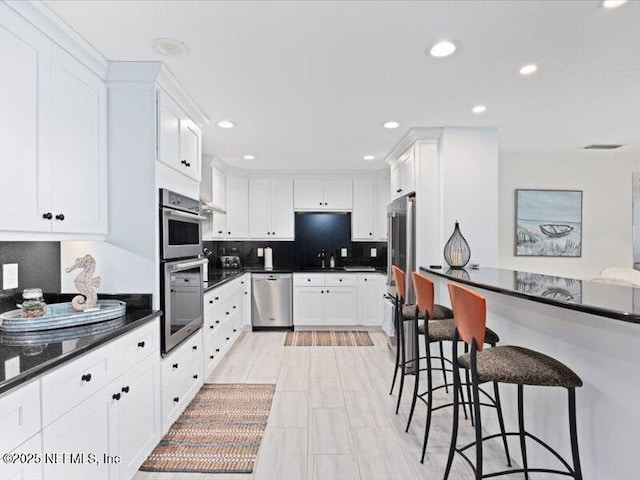 kitchen featuring white cabinets, a kitchen breakfast bar, sink, decorative backsplash, and stainless steel appliances