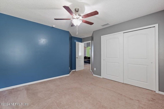 unfurnished bedroom with light carpet, a textured ceiling, a closet, and ceiling fan