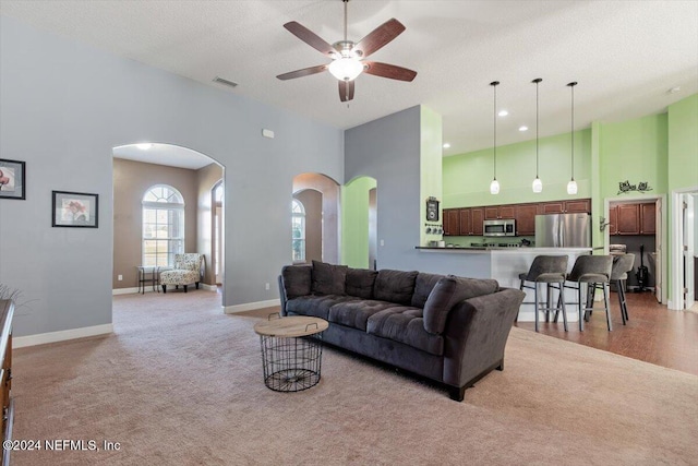 living room featuring light carpet, a textured ceiling, a towering ceiling, and ceiling fan