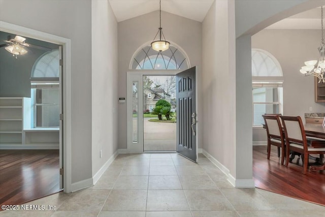 tiled foyer entrance with ceiling fan with notable chandelier and high vaulted ceiling