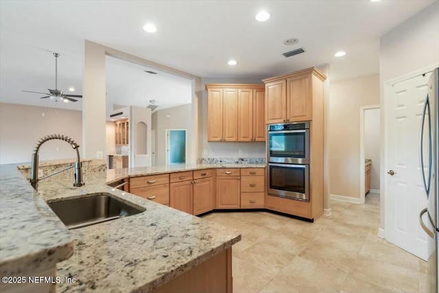 kitchen featuring kitchen peninsula, light stone counters, sink, and appliances with stainless steel finishes