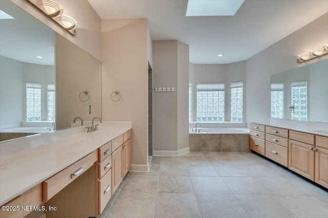 bathroom with tile patterned floors, a skylight, vanity, and a relaxing tiled tub