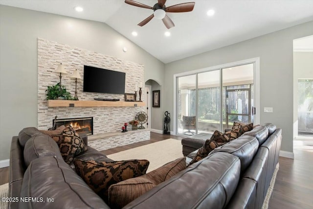 living room with ceiling fan, dark hardwood / wood-style floors, a stone fireplace, and lofted ceiling