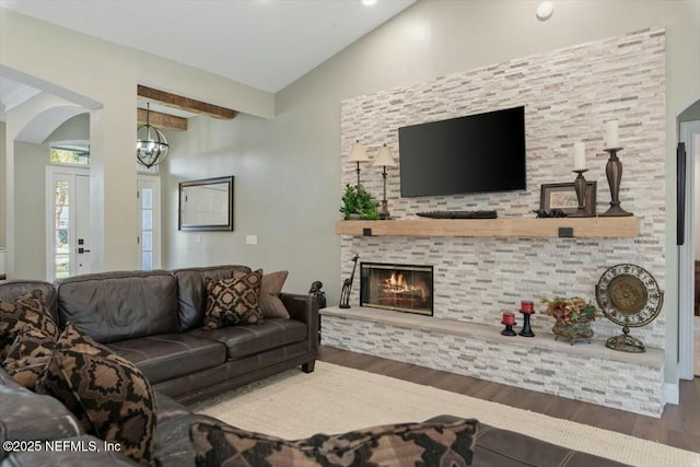 living room featuring hardwood / wood-style floors, vaulted ceiling with beams, a stone fireplace, and a notable chandelier