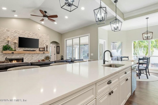 kitchen featuring ceiling fan, sink, white cabinetry, hanging light fixtures, and a stone fireplace