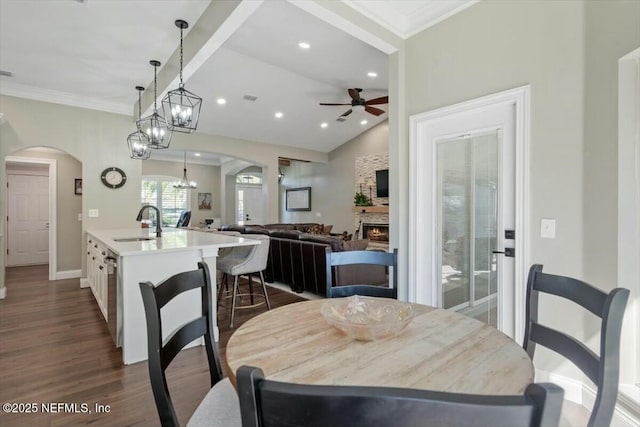 dining space featuring ceiling fan, sink, dark hardwood / wood-style flooring, vaulted ceiling, and a fireplace