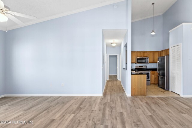 kitchen featuring a high ceiling, light wood-type flooring, decorative light fixtures, appliances with stainless steel finishes, and ornamental molding