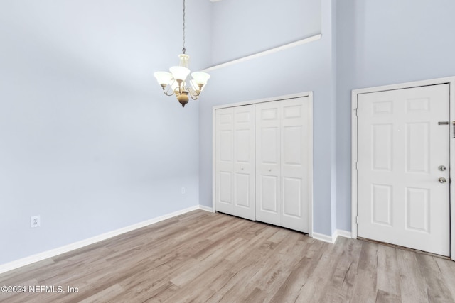 unfurnished bedroom featuring a closet, a chandelier, a high ceiling, and light hardwood / wood-style flooring