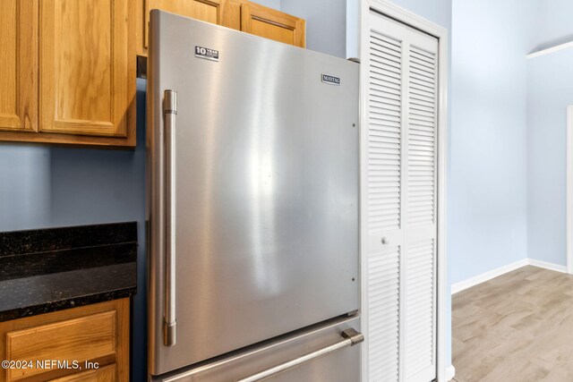 kitchen with high quality fridge, dark stone countertops, and light hardwood / wood-style floors