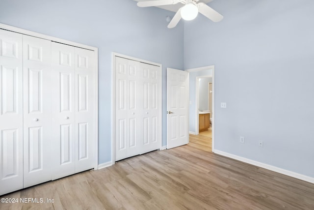 unfurnished bedroom featuring a towering ceiling, light wood-type flooring, two closets, and ceiling fan