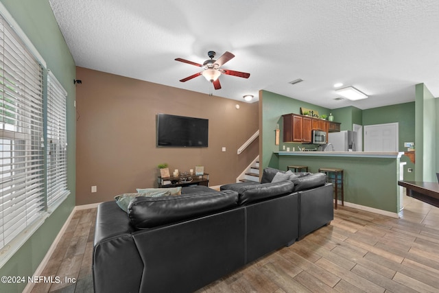 living room featuring a textured ceiling, light hardwood / wood-style floors, and ceiling fan