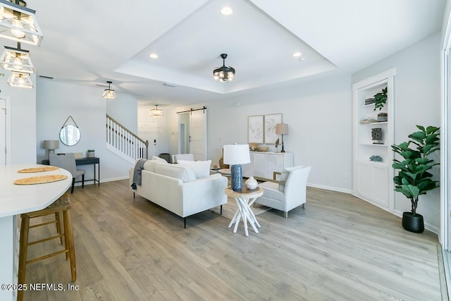 living room featuring a barn door, a tray ceiling, built in features, and light hardwood / wood-style floors