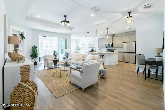 living room with a raised ceiling, sink, and light hardwood / wood-style flooring