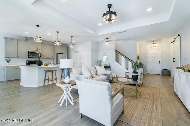 living room featuring a barn door, a tray ceiling, and light hardwood / wood-style flooring