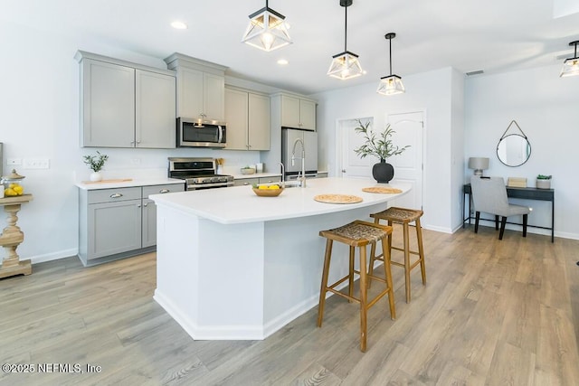 kitchen with gray cabinetry, stainless steel appliances, a kitchen island with sink, and light hardwood / wood-style flooring