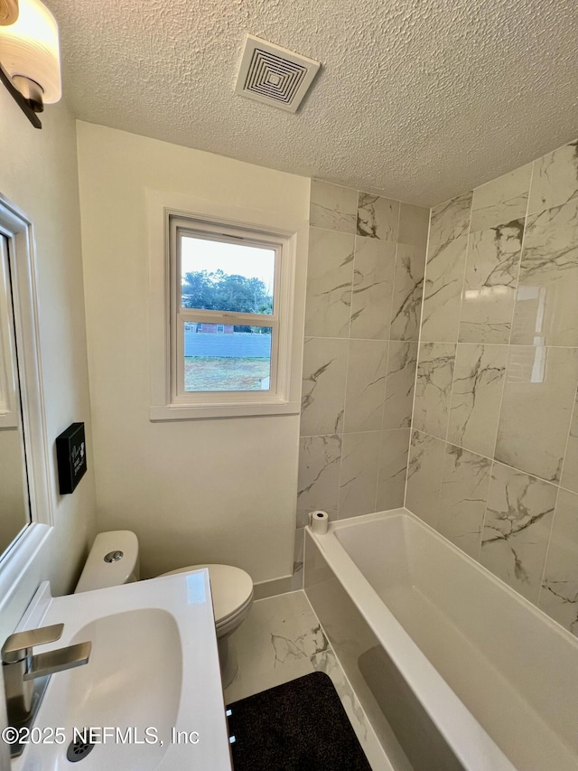 full bathroom featuring tiled shower / bath, toilet, sink, and a textured ceiling