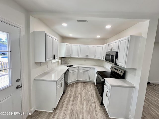 kitchen with sink, light wood-type flooring, white cabinets, and appliances with stainless steel finishes