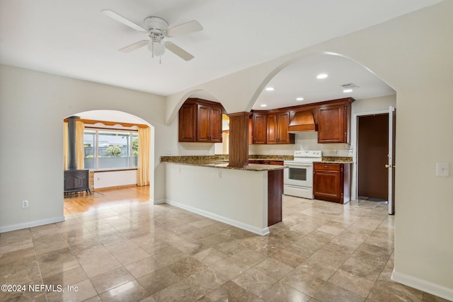 kitchen with kitchen peninsula, custom exhaust hood, white range with electric stovetop, ceiling fan, and stone counters