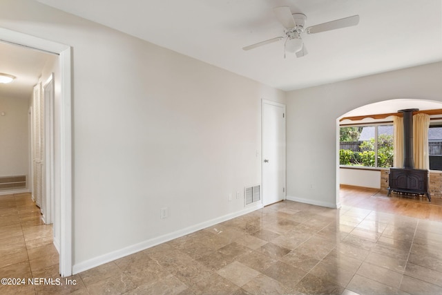 unfurnished room featuring ceiling fan and a wood stove