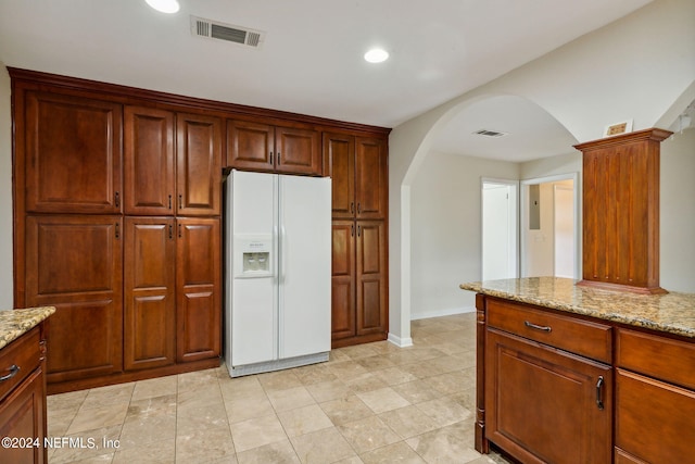 kitchen featuring light stone countertops and white refrigerator with ice dispenser