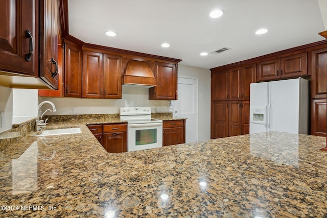 kitchen with stone counters, custom range hood, white appliances, and sink