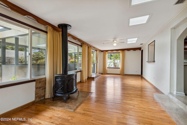 unfurnished living room with light wood-type flooring, a wood stove, ceiling fan, and ornamental molding