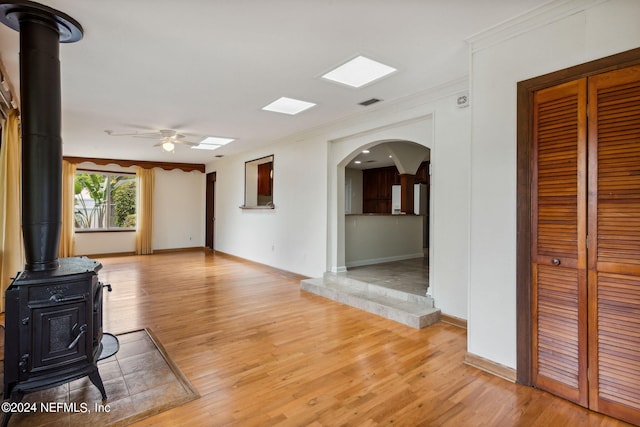 unfurnished living room featuring light hardwood / wood-style floors, a wood stove, ceiling fan, and ornamental molding