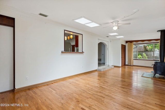 unfurnished living room with light wood-type flooring, a wood stove, ceiling fan, and ornamental molding