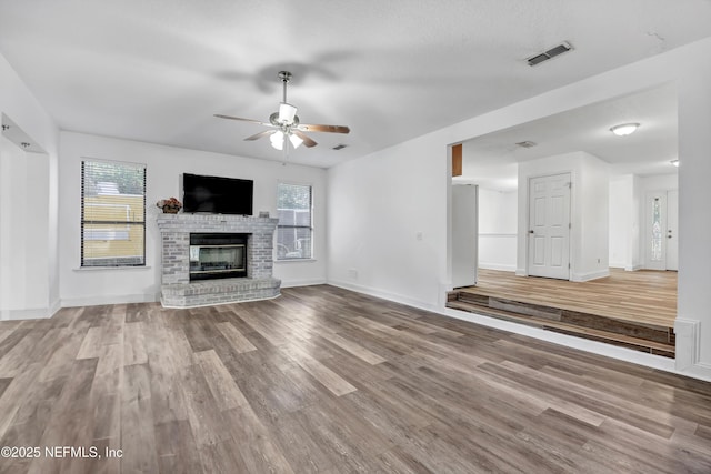 unfurnished living room featuring ceiling fan, light hardwood / wood-style flooring, plenty of natural light, and a brick fireplace