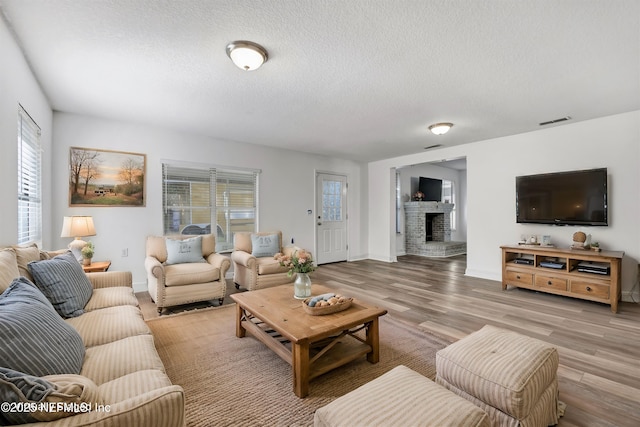 living room with a textured ceiling, light hardwood / wood-style floors, and a brick fireplace