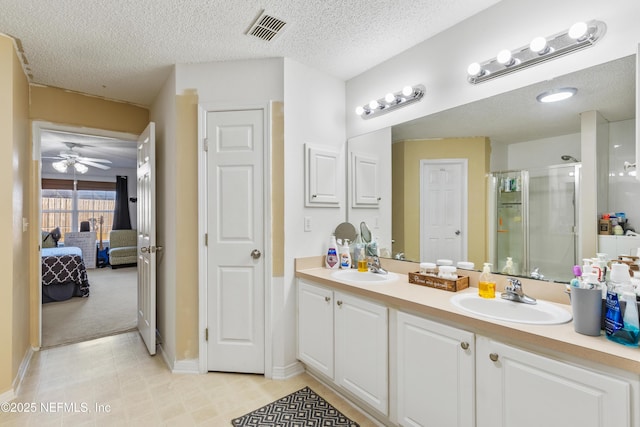 bathroom with a textured ceiling, ceiling fan, vanity, and an enclosed shower