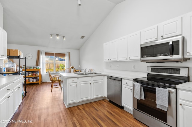 kitchen featuring white cabinets, sink, vaulted ceiling, appliances with stainless steel finishes, and kitchen peninsula